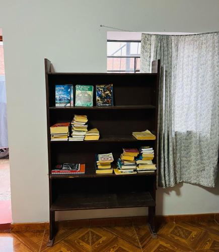 a book shelf filled with books next to a window at hostel arcoiris urubamba in Urubamba