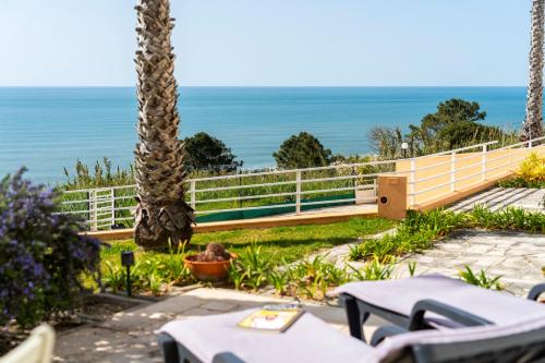 a patio with tables and palm trees and the ocean at Nativo Big Wave Front Row - 1BR in Nazaré