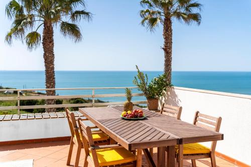 a wooden table and chairs on a balcony with palm trees at Nativo Big Wave Front Row 2BR Nazaré in Nazaré