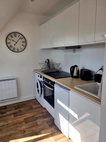 une cuisine avec des placards blancs et une horloge murale dans l'établissement Studio à côté de la thalasso, à Cabourg