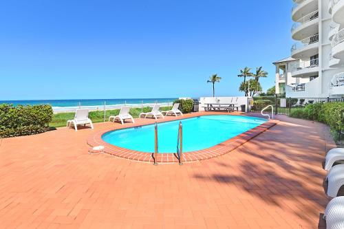 a swimming pool with chairs and the ocean in the background at Albatross North Apartments in Gold Coast