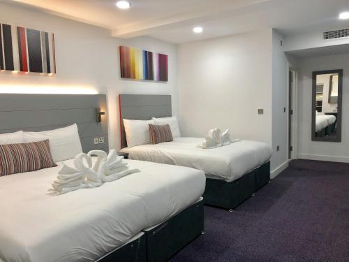 a hotel room with two beds and a mirror at Ilford Hotel Goodmayes in Ilford