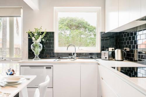 a white kitchen with a window and a sink at Renovated Retro Apartment Near Harbour Front Walks in Sydney