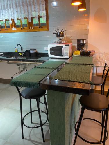 a kitchen with a counter with stools and a microwave at Casa Aconchegante na Montanha in Campos do Jordão