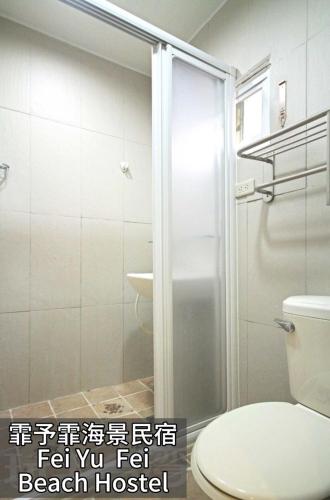 a bathroom with a toilet and a glass shower door at Fei Yu Fei Beach Hostel in Lanyu