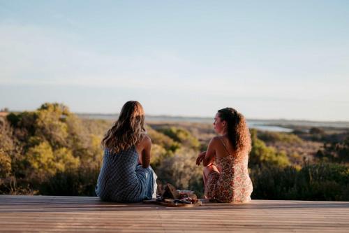 Deux femmes sont assises sur une passerelle en bois. dans l'établissement Waterfront Luxury Villa- Private, Nature, Island, à Hindmarsh Island