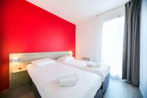two beds in a room with a red wall at Comfort Aparthotel Toulouse Métropole in Toulouse