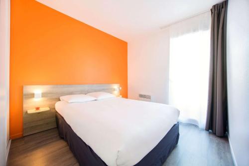 a large white bed in a room with an orange wall at Comfort Aparthotel Toulouse Métropole in Toulouse
