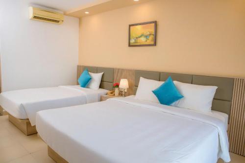 two beds in a hotel room with blue pillows at Lanxy Hotel Nha Trang in Nha Trang