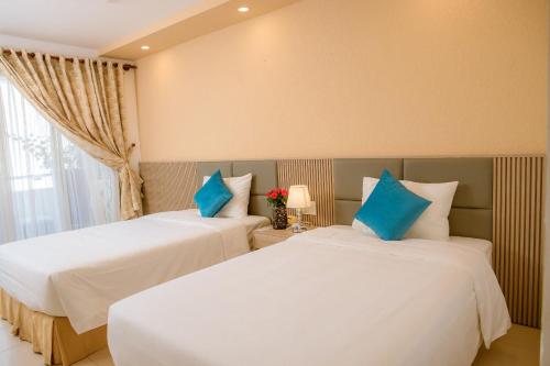 two beds in a hotel room with blue pillows at Lanxy Hotel Nha Trang in Nha Trang
