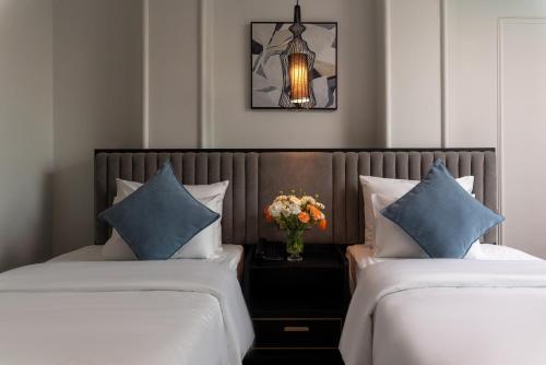 two beds with blue pillows and a vase of flowers at 22 Land Hotel in Hanoi