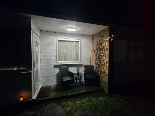 a patio with two chairs and a table at night at Roma's Retreat chalet, Hemsby in Hemsby