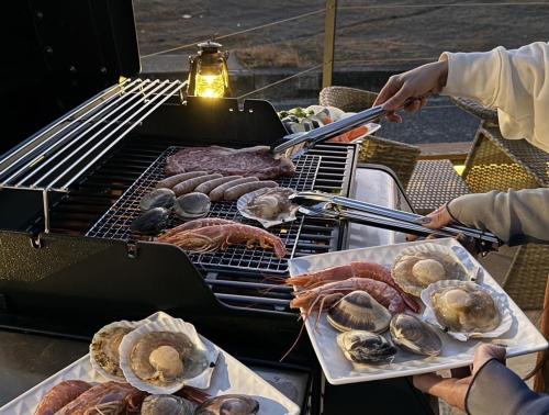 a person cooking meat and seafood on a grill at H&H Calme in Minamiboso