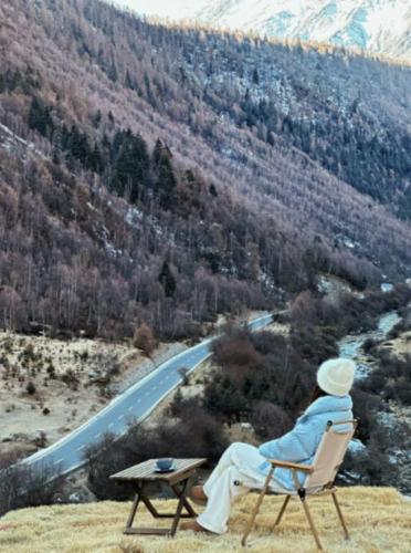 a person sitting in a chair looking at a mountain at Mount Sigunian Looking up at the snowy peak Vacilando Hotel in Mount Siguniang