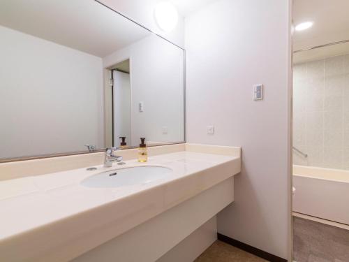 a white bathroom with a sink and a mirror at ART HOTEL Kashima Central in Kamisu
