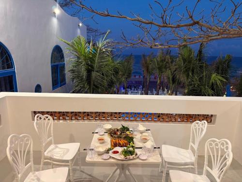 a table with white chairs and food on a balcony at KParis Beach Resort in Bình Sơn