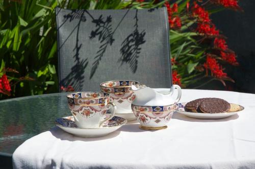 a table with four cups and a teapot and cookies at Cosy Seaside Cottage Baltimore in Ballylinchy