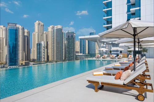 a pool with chairs and umbrellas on a building at 1BR Gem with Stunning Marina Views, Close to Metro in Dubai