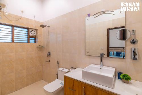 a bathroom with a sink and a toilet and a mirror at StayVista at Leela Retreat with BBQ, Bonfire, Pool & Lawn in Sohna