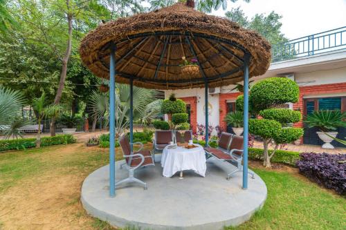 a table and chairs under an umbrella in a yard at StayVista at Leela Retreat with BBQ, Bonfire, Pool & Lawn in Sohna