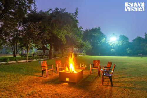a group of chairs around a fire in a field at StayVista at Leela Retreat with BBQ, Bonfire, Pool & Lawn in Sohna