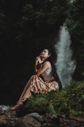 a woman sitting on the ground in front of a waterfall at Glamping tent in Pelaga Eco Park in Patjung