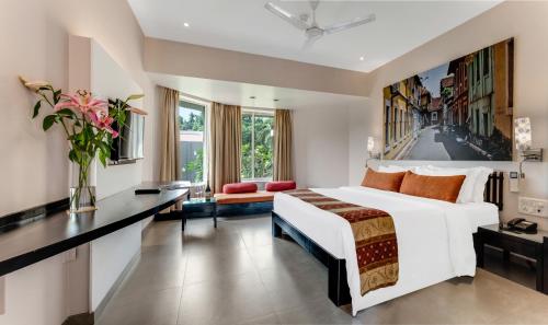 a bedroom with a large white bed and a desk at Whispering Palms Beach Resort in Candolim