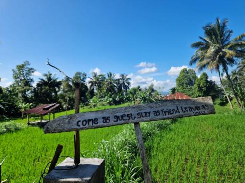 a sign in a field with a palm tree in the background at Ariel Bungalow Tetebatu in Tetebatu