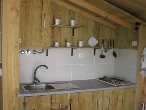 una cocina con armarios de madera, fregadero y utensilios de cocina en African Tent, en Ponte da Barca