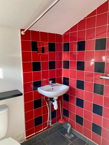 La salle de bains est pourvue de carrelage rouge, d'un lavabo et de toilettes. dans l'établissement La petite maison rouge, à Cucq