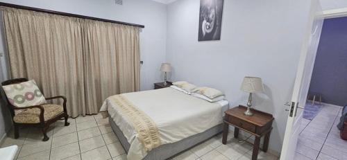 een slaapkamer met een bed, een stoel en een raam bij Meerensee Cottage in Richards Bay