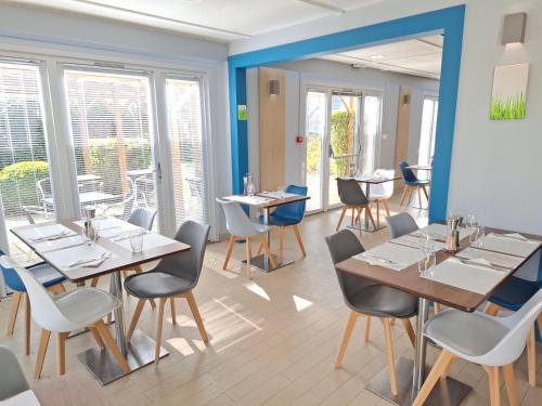 a dining room with tables and chairs and windows at Campanile Versailles Buc in Buc