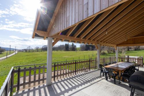 a covered deck with a table and chairs and a field at Gîte "La Partie de Bise", 12 personnes in Le Barboux