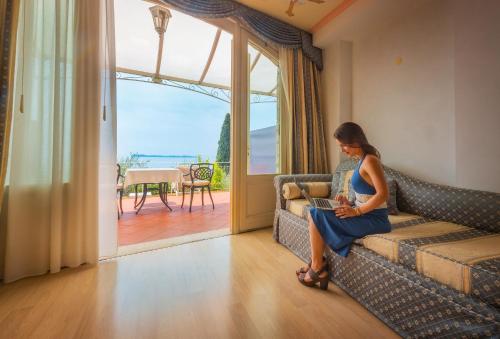 a woman sitting on a couch in a living room at Hotel Villa Florida & Suite Apartments in Gardone Riviera