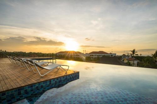 a pool with lounge chairs and the sunset in the background at ARTOTEL Sanur Bali in Sanur