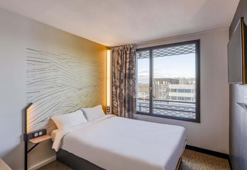 a hotel room with a bed and a large window at B&B HOTEL Bordeaux Bassins à flot in Bordeaux