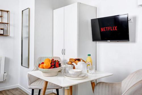 - une table blanche avec un bol de fruits et une télévision dans l'établissement Studio Cosy au coeur de Paris pres des Buttes-Chaum, à Paris