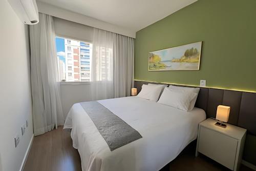 Un dormitorio con una gran cama blanca y una ventana. en Apto charmoso Gleba Palhano, en Londrina