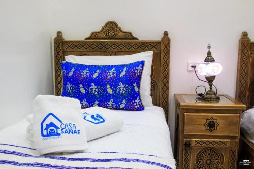a bed with a blue and white pillow and a night stand at Casa Sanae in Chefchaouene