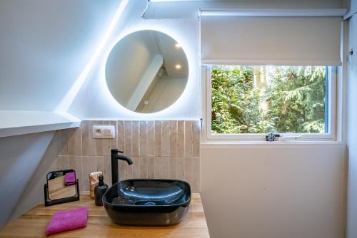a bathroom with a round mirror and a black tub at Boshuisje Rekem - Ignis in Lanaken