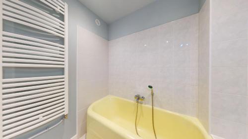 La salle de bains blanche est pourvue d'une baignoire jaune et d'une fenêtre. dans l'établissement L'atelier de la rue Mailly, à Perpignan