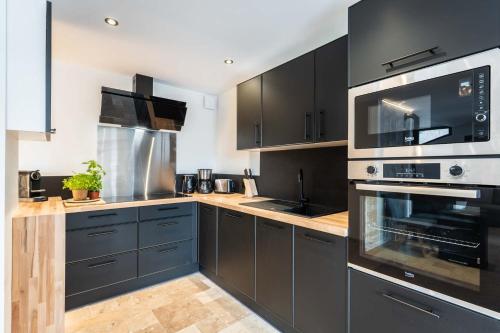 une cuisine avec des armoires noires et des appareils en acier inoxydable dans l'établissement Linea Loft - La Plagne Paradiski, à La Plagne Tarentaise