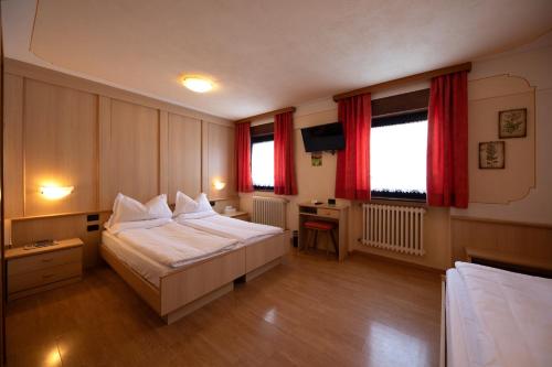 a bedroom with a bed and a desk and two windows at Albergo Venezia in Passo Rolle