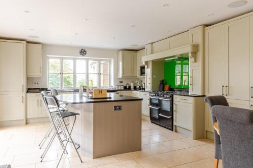 a kitchen with white cabinets and an island with chairs at Spacious farmhouse with stunning valley views in Woodchester