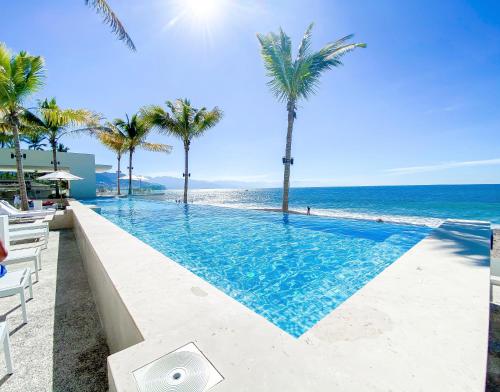 a swimming pool next to the beach with palm trees at Harbor 171 - LOFT- 10th floor- Beach Front Puerto Vallarta in Puerto Vallarta