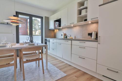 a kitchen with white cabinets and a wooden table at Süderdünengarten in Langeoog