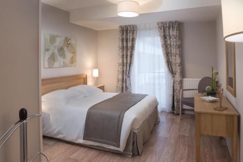 a bedroom with a bed and a desk and a window at Domitys Les Gréements d'Or - résidence séniors in Douarnenez