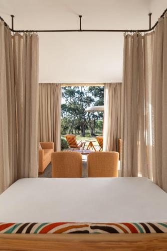 a bedroom with a bed and chairs and a window at Praia do Canal Nature Retreat - Small Luxury Hotels of the World in Aljezur