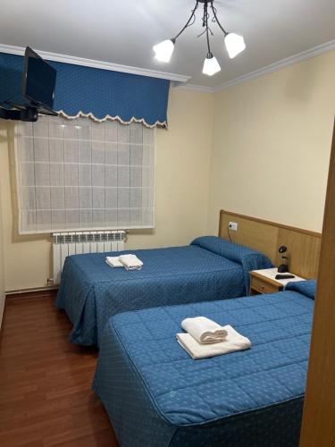 two beds in a room with blue sheets and towels at Pensión Arcano in Arzúa