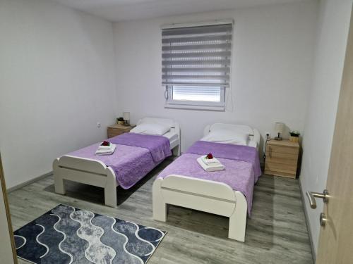 two beds in a room with purple sheets and a window at Apartman Pranić Mostar in Mostar
